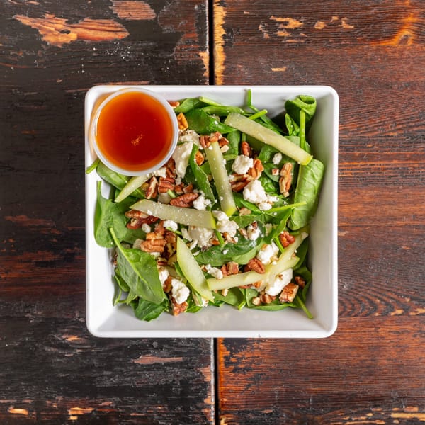Spinach salad with pecans, feta cheese, green apple slices, and a side of dressing.