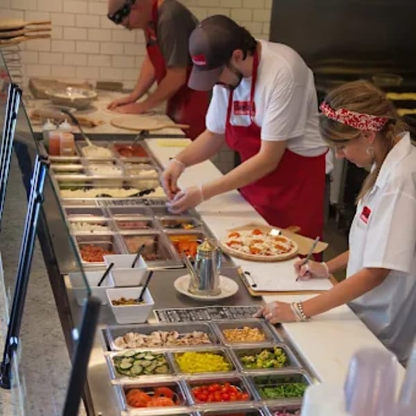 Bambino's Urban Pizzeria staff preparing pizzas with fresh toppings at a counter.