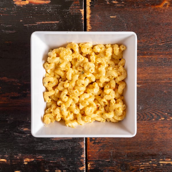 A white square bowl filled with creamy macaroni and cheese on a rustic wooden table.