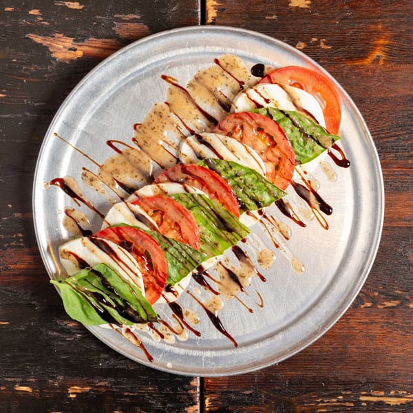 Caprese salad with fresh mozzarella, tomatoes, basil, and balsamic glaze on a metal plate.