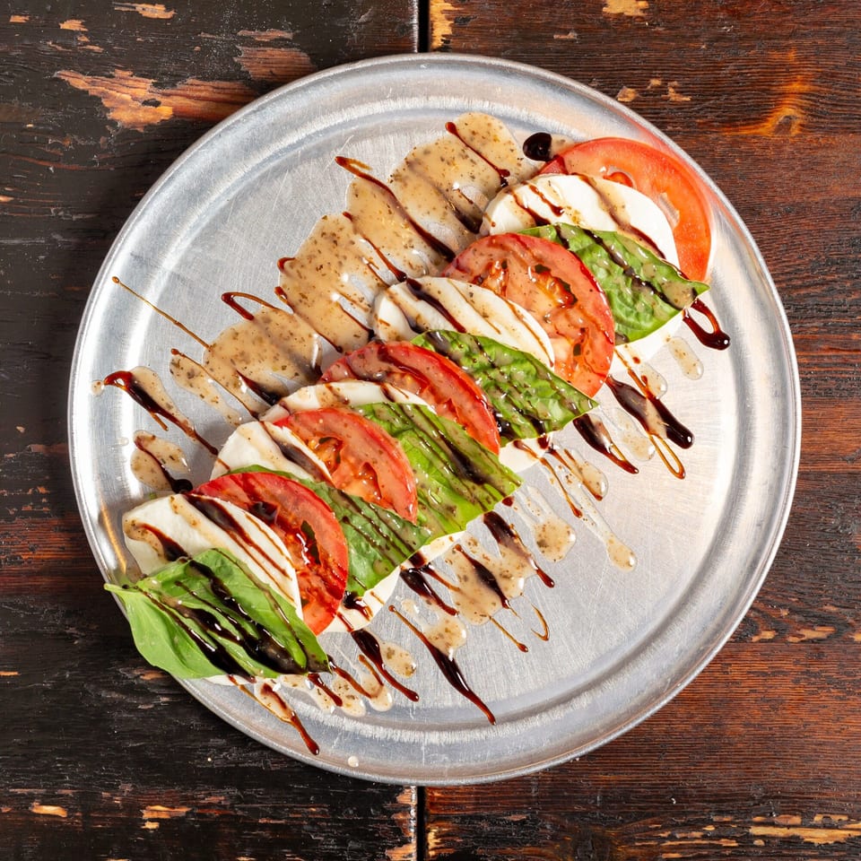 Caprese salad with fresh mozzarella, tomatoes, basil, and balsamic glaze on a metal plate.